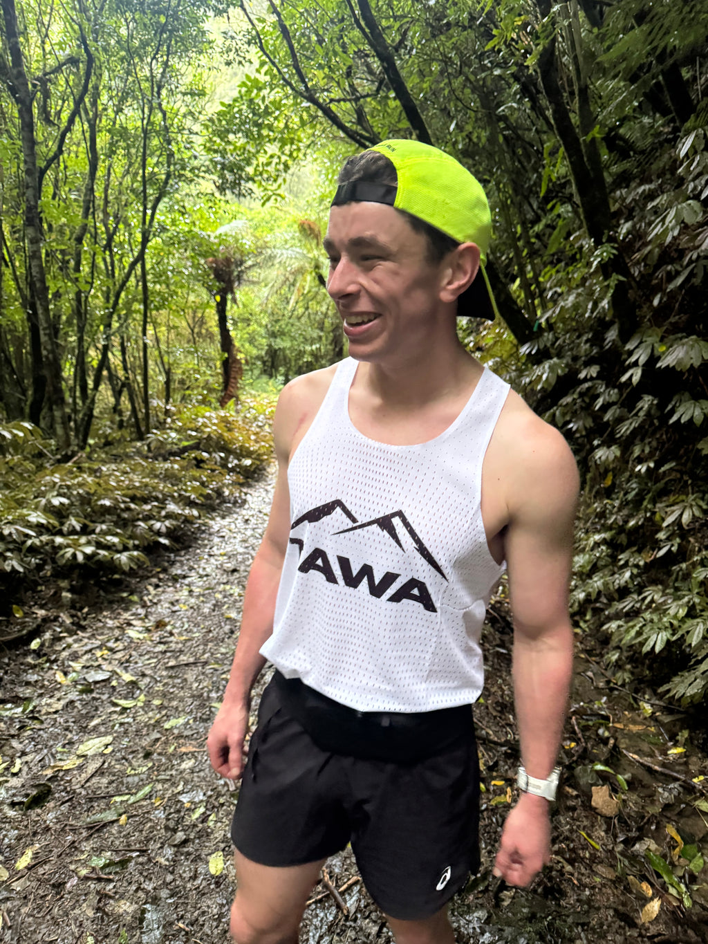 Person wearing a white tank top with 'Tawa' logo in a forest setting